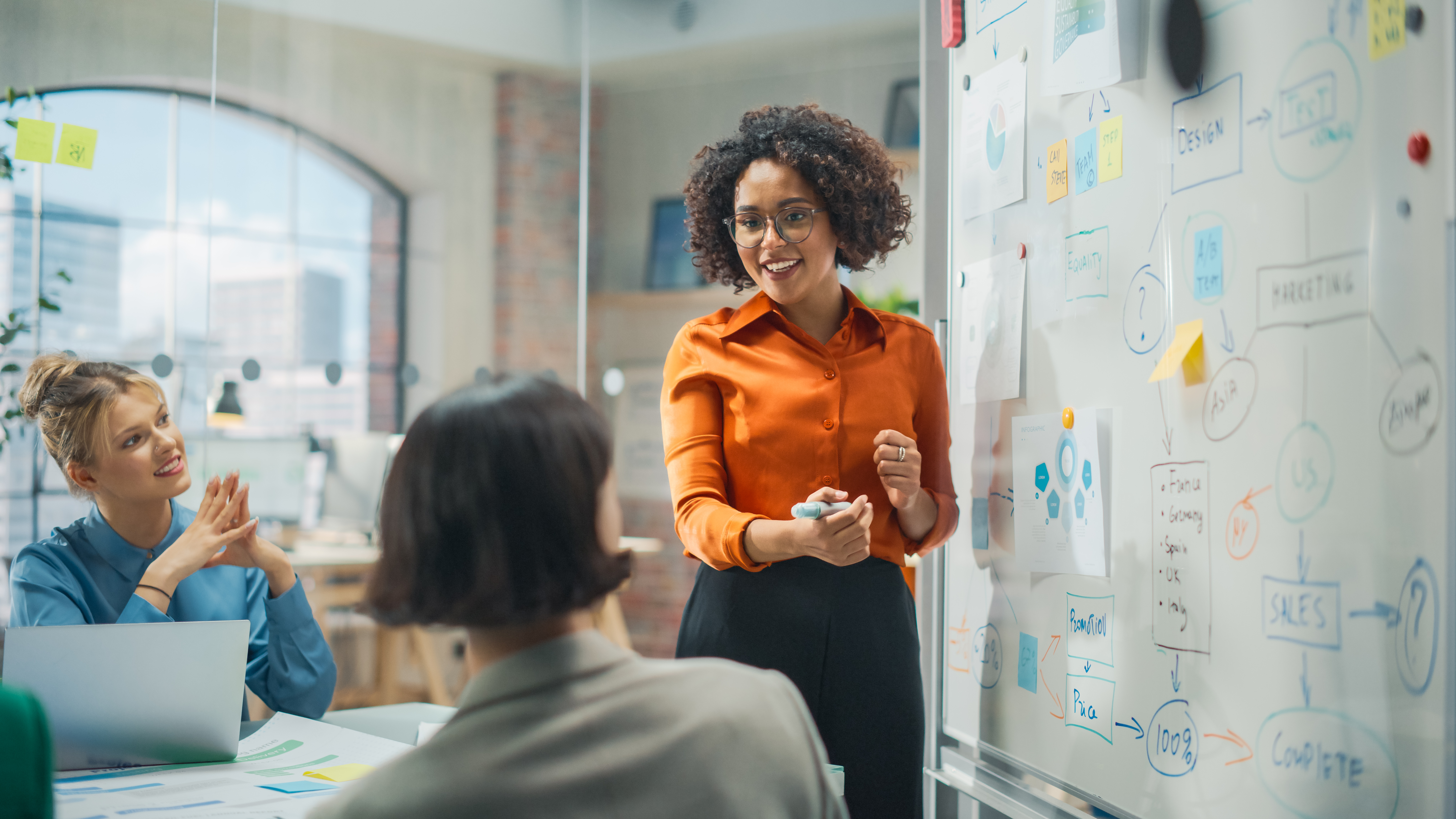 woman-presenter-at-whiteboard-giving-team-presentation.jpeg
