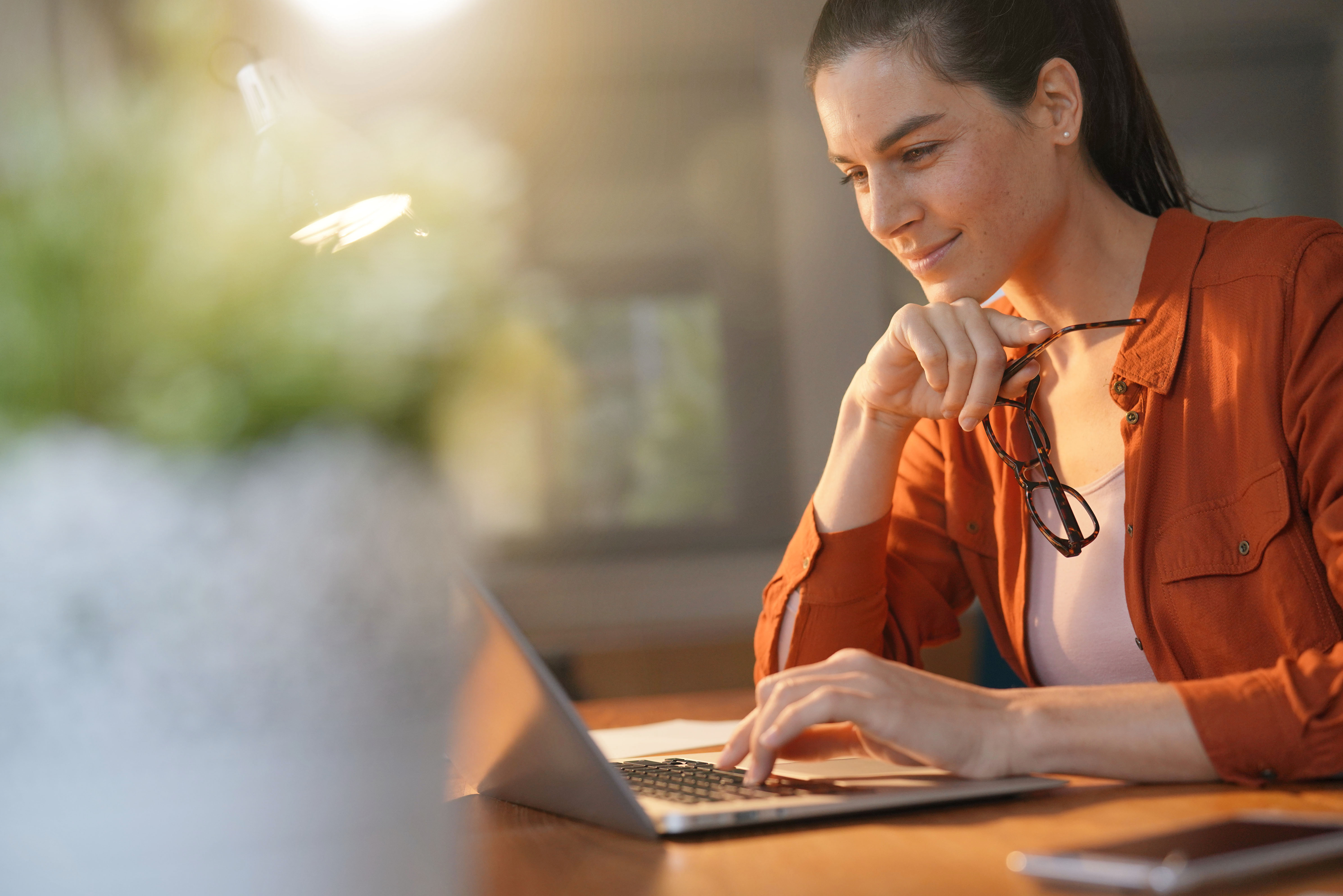 smiling-woman-in-orange-shirt-working-on-laptop-with-warm-light.jpeg