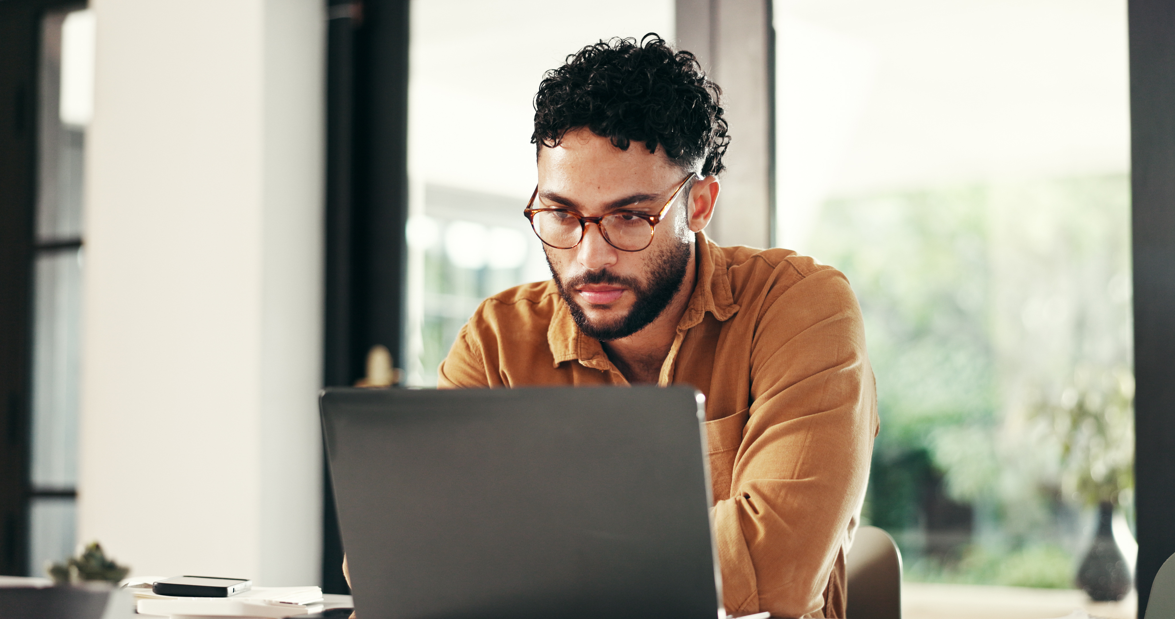 bearded-man-with-glasses-focused-on-laptop-at-home-desk.jpeg