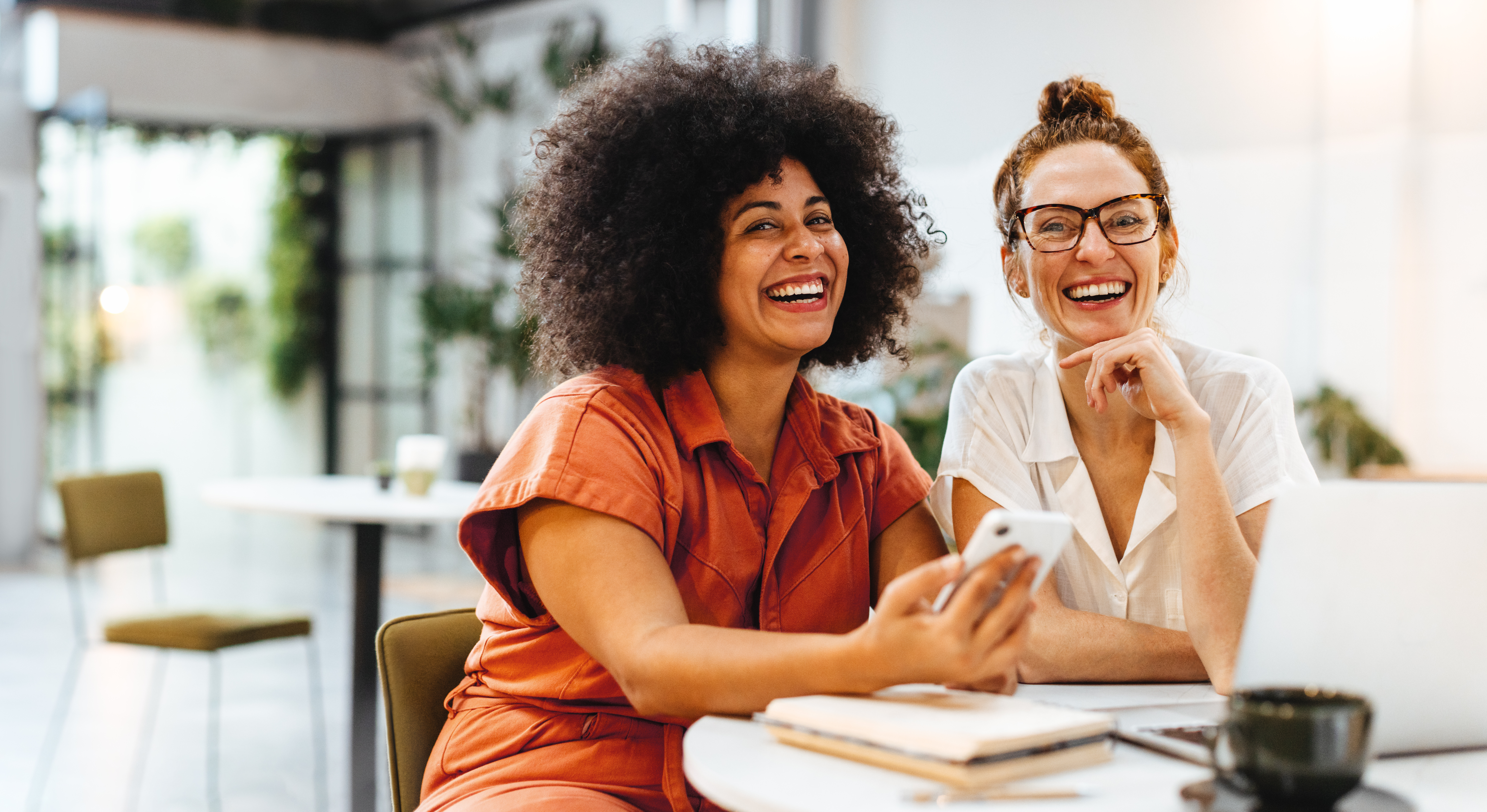 two-women-laughing-together-at-office-table-with-phone.jpeg