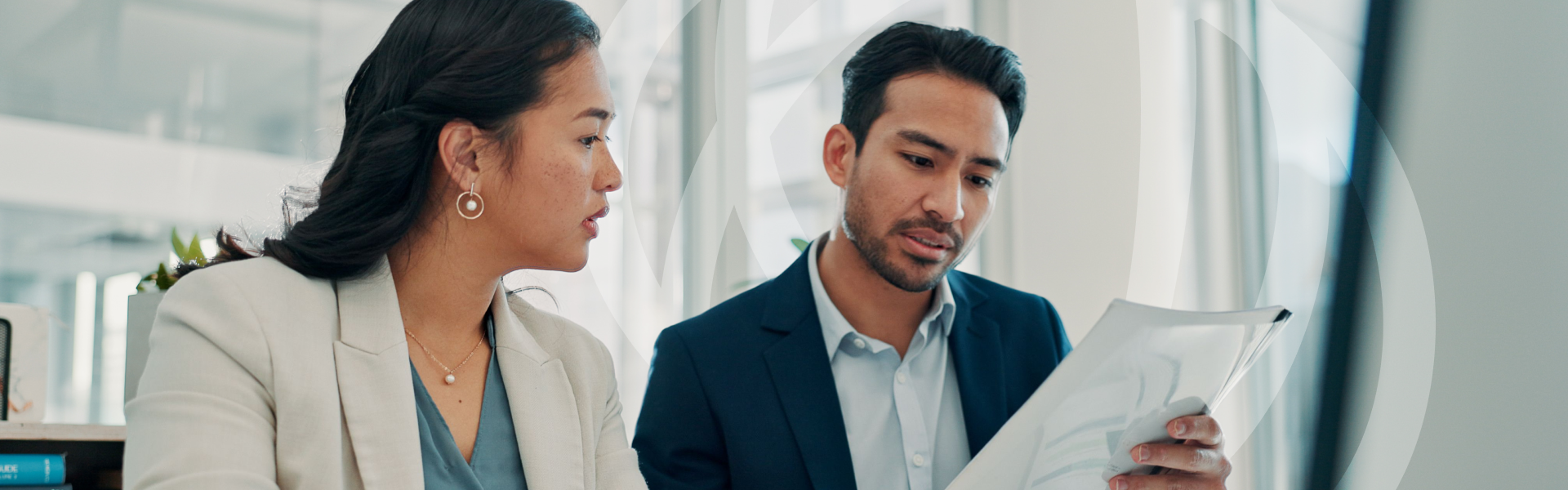 Two colleagues (a man and a woman) reviewing a document together at a desk in a modern office.