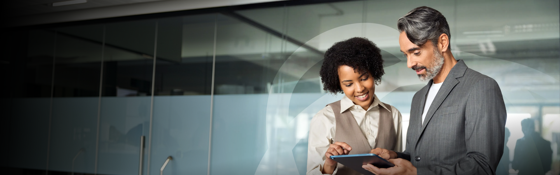 A woman and a man reviewing a tablet in a modern office with glass walls and doors.